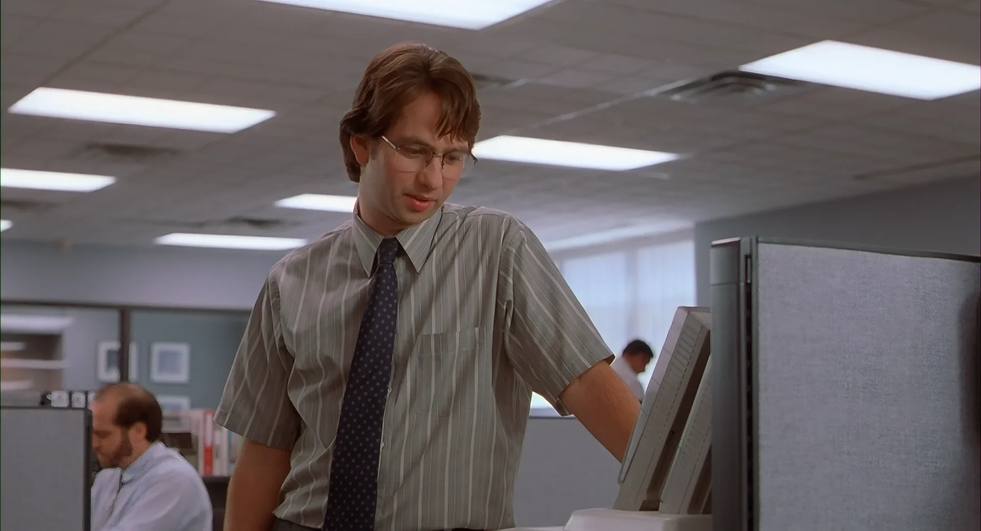 Milton staring at a printer in a fluorescent cubicle farm, trying to make sense of the error.