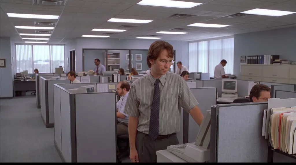 Peter standing in a cubicle farm, one hand on a beige CRT monitor.