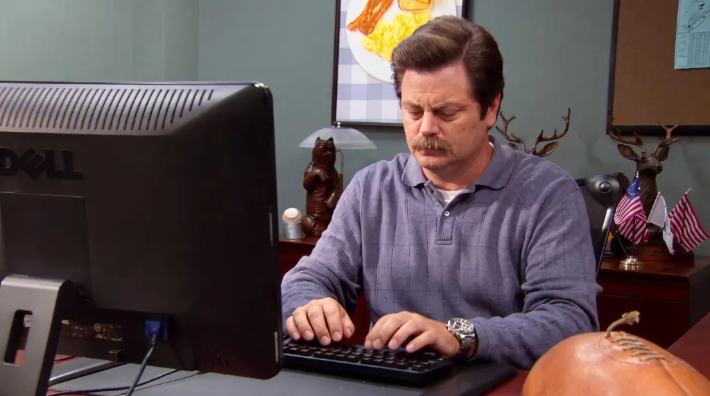 Ron Swanson at his desk, suspicious of the monitor.